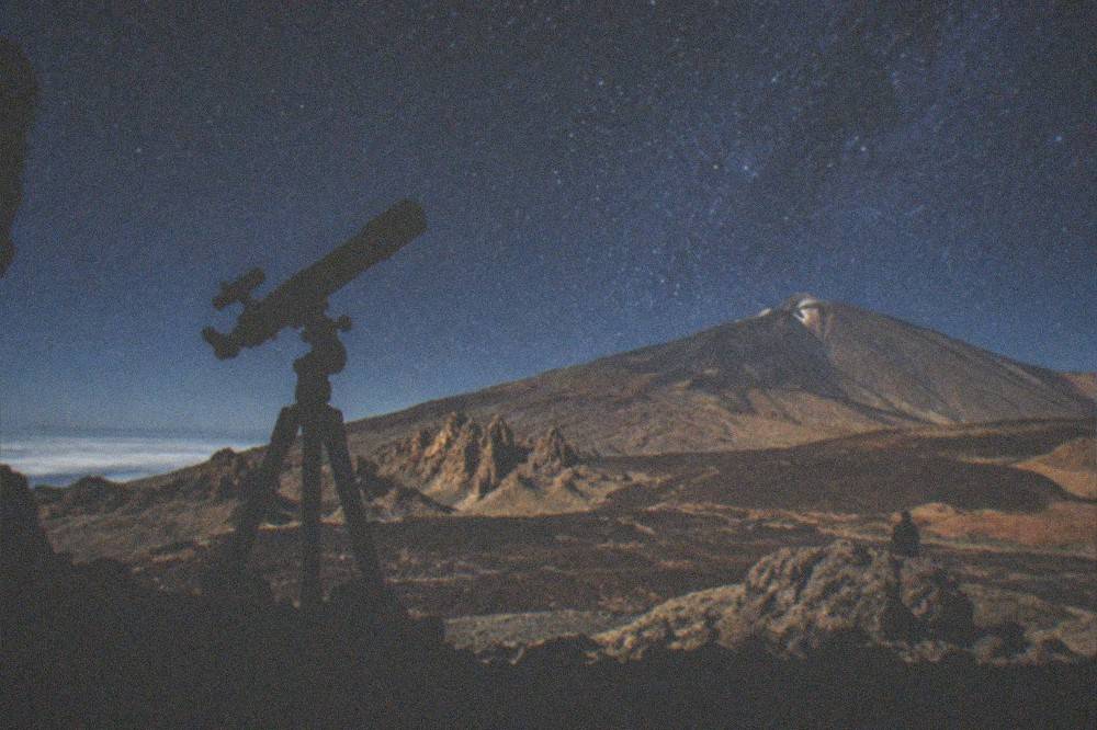 A telescope silhouette against a star-filled sky above the volcanic slopes of Teide