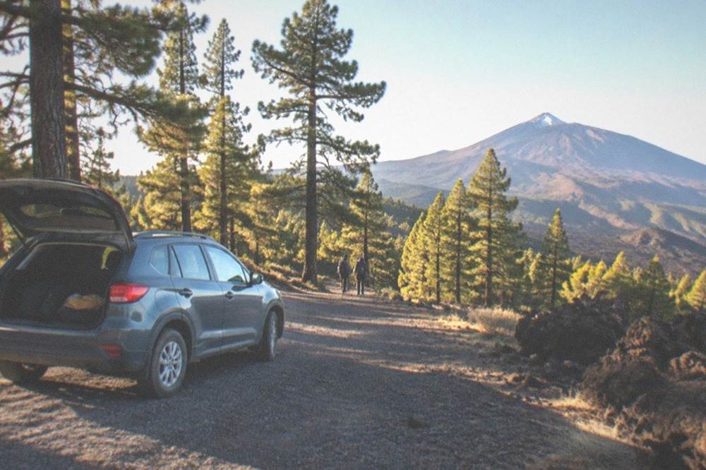 A parked car at a gravel pull-in beside a pine forest track high on the mountain