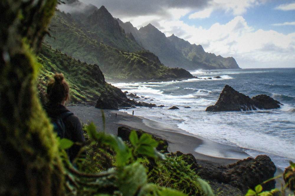 Waves breaking onto a dark sand cove with rocky headlands on either side