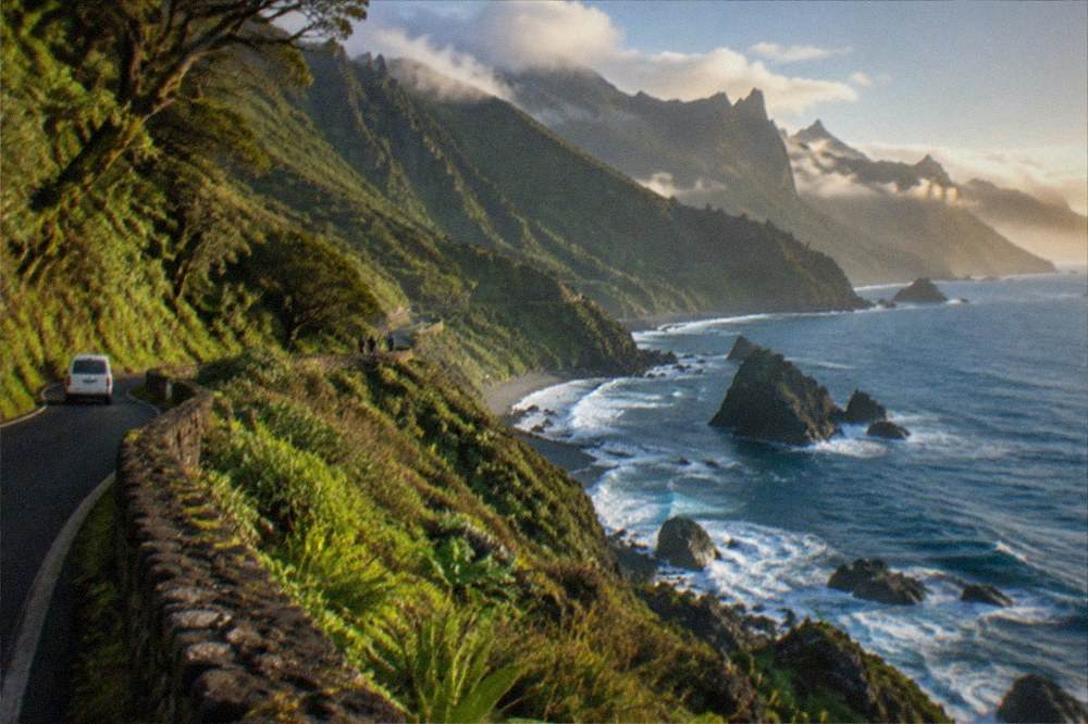 A coastal road with stone walls and green slopes descending to the sea