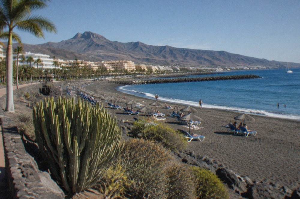 A wide pale-sand beach in Costa Adeje with sun loungers, parasols and calm blue water