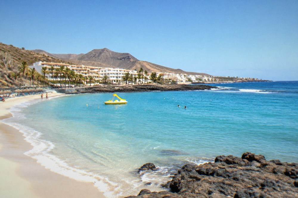 Calm turquoise water at the shoreline of a resort beach with parasols and a pedal boat