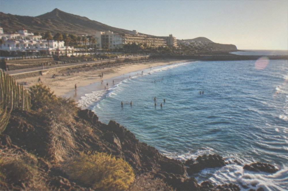 Sunlit resort beach in winter with people in the water and hotel terraces behind