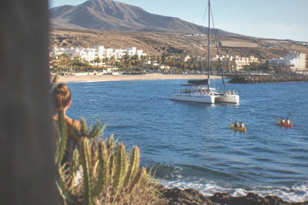 A catamaran and kayaks on calm water off a resort coastline