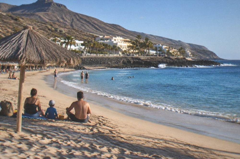 A family on a resort beach with a parasol near calm shallow water