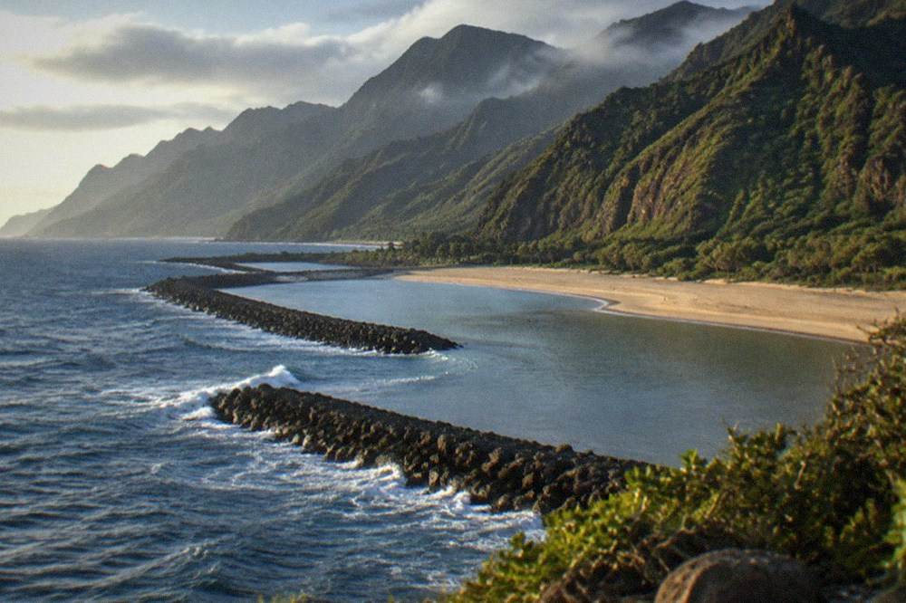 Stone breakwaters running parallel to a sandy beach with calm water between them and the shore