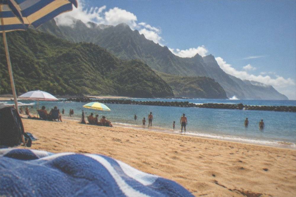 Families with umbrellas on golden sand beside calm, shallow water