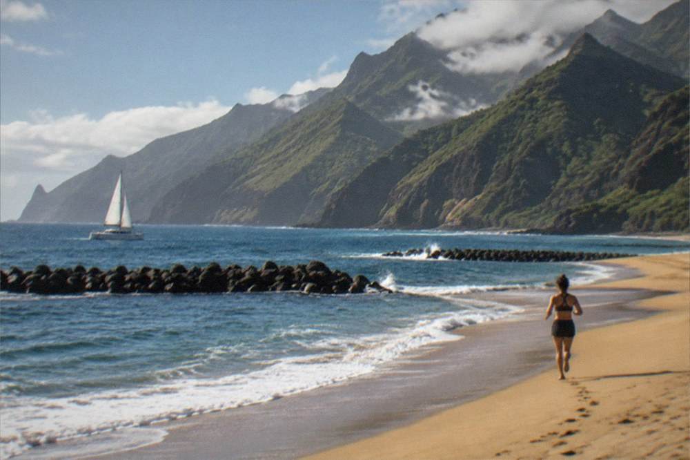 A catamaran under sail on open water near dark volcanic cliffs