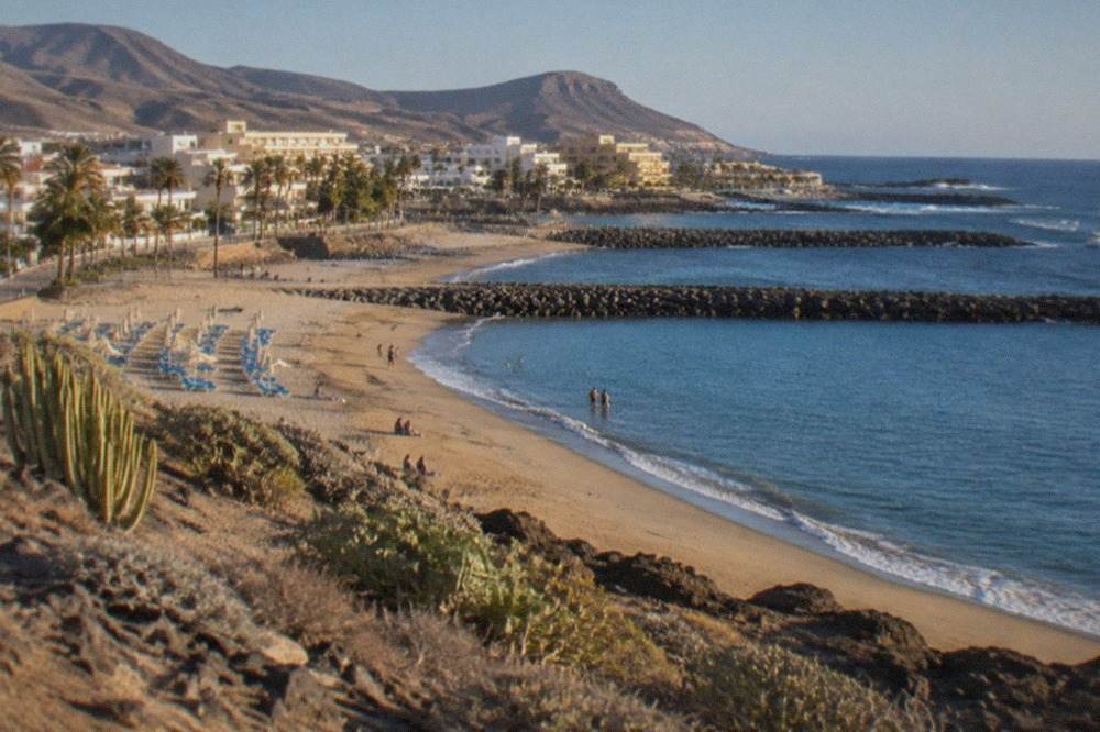 Golden sandy beach with calm water behind breakwaters and sunbeds under a clear sky