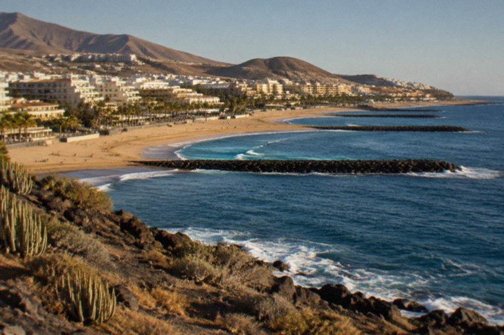 Wide view of a golden beach with breakwaters in the sea and apartment blocks behind the promenade