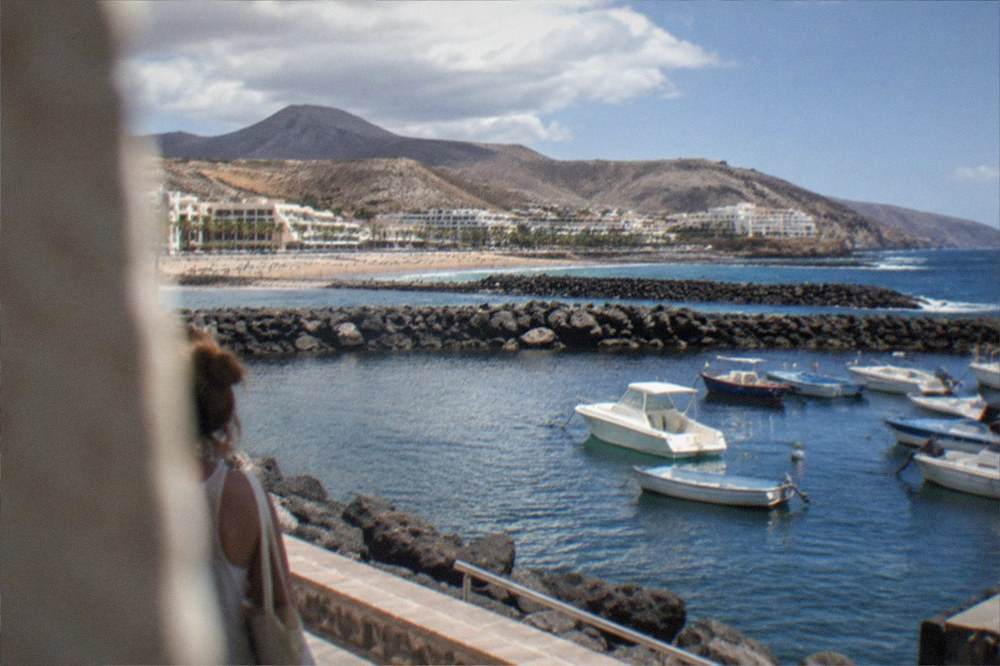 Boats moored in a harbour with a beach and hills in the background