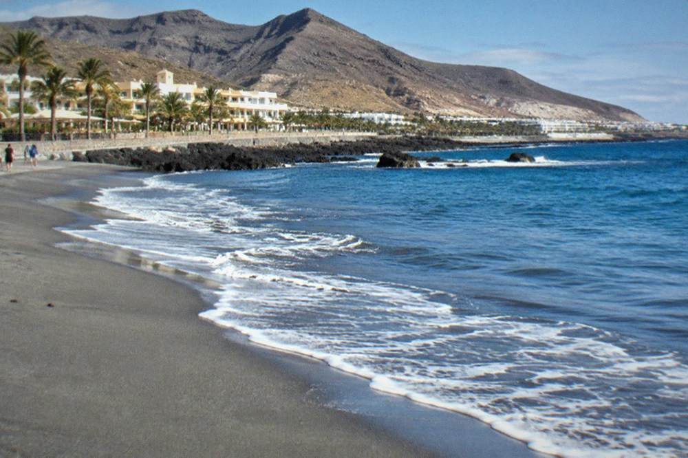 Close view of grey volcanic sand with a gentle line of surf