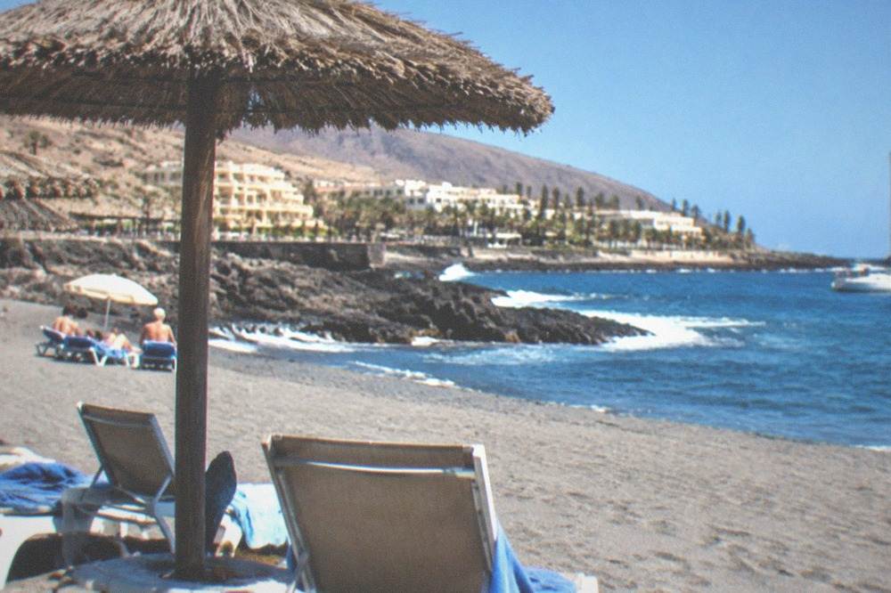 Sun loungers and parasols on grey sand under a clear blue sky