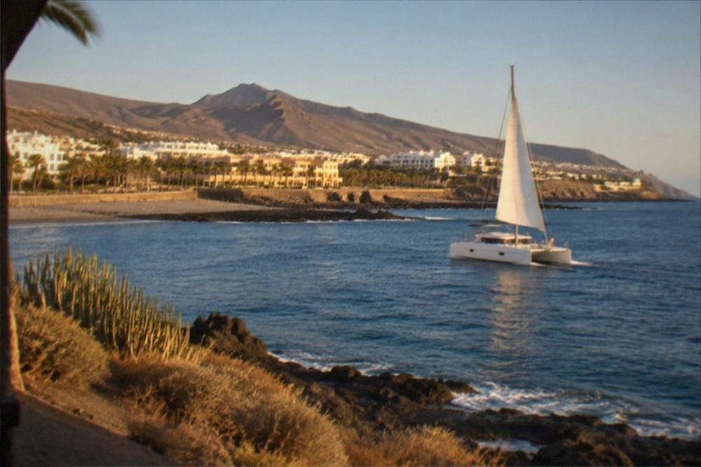A catamaran under way on calm blue water near the coast