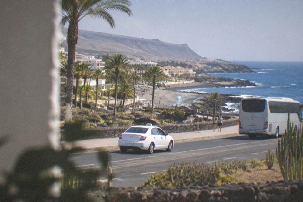 A white taxi and a bus on a sunny resort road with palm trees