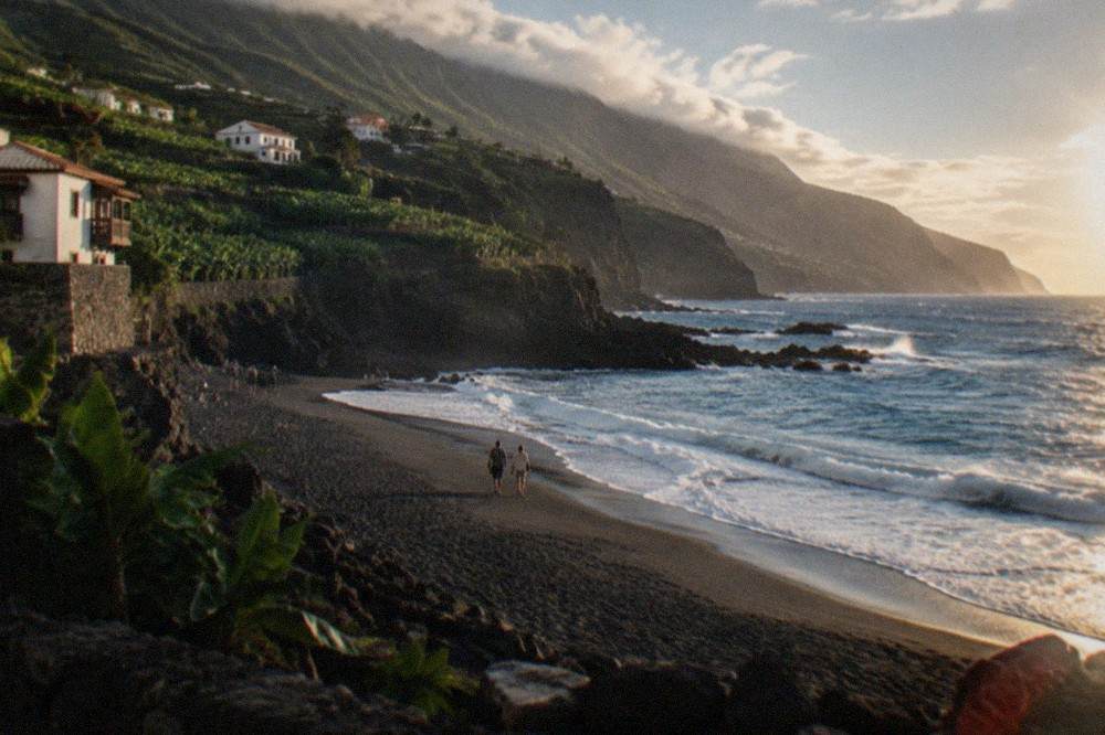 Dark volcanic sand and Atlantic waves along a cliff-backed shoreline