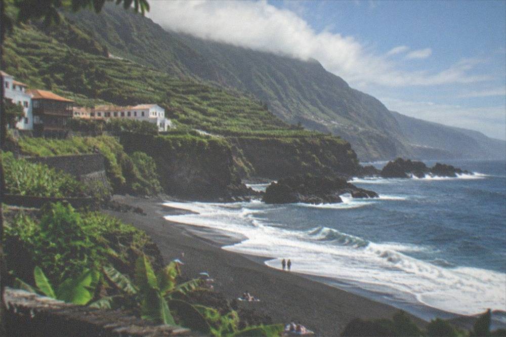 Waves breaking on dark sand with green cliffs rising behind the beach