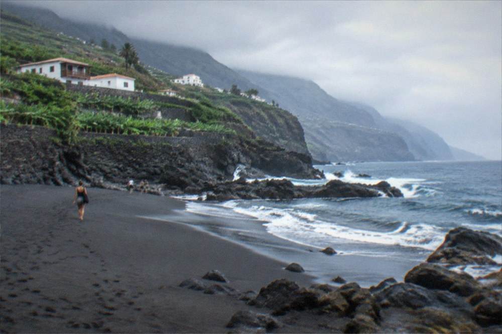 A broad dark beach at low tide with cliffs and a hazy horizon