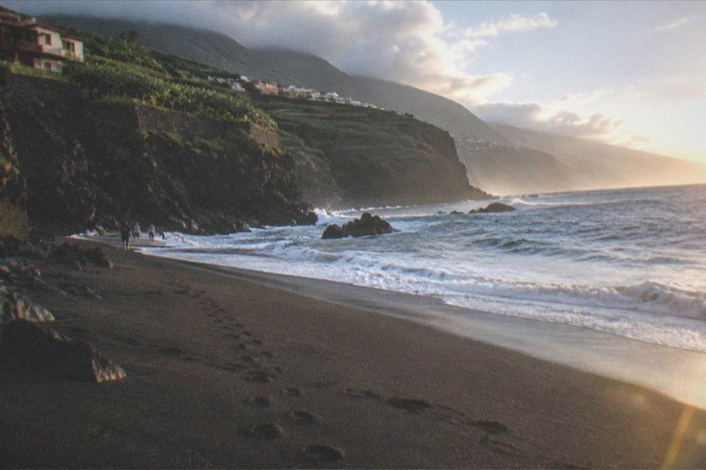 Footprints crossing dark sand toward the surf line under a cliff