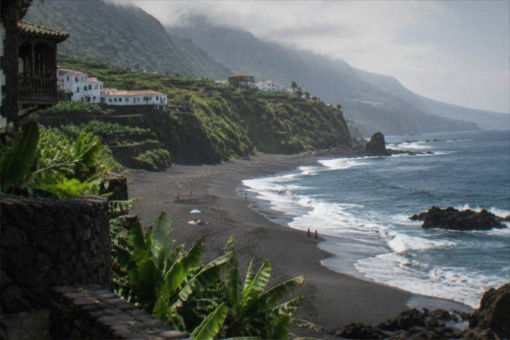 A long curve of dark sand between a green cliff and the Atlantic Ocean
