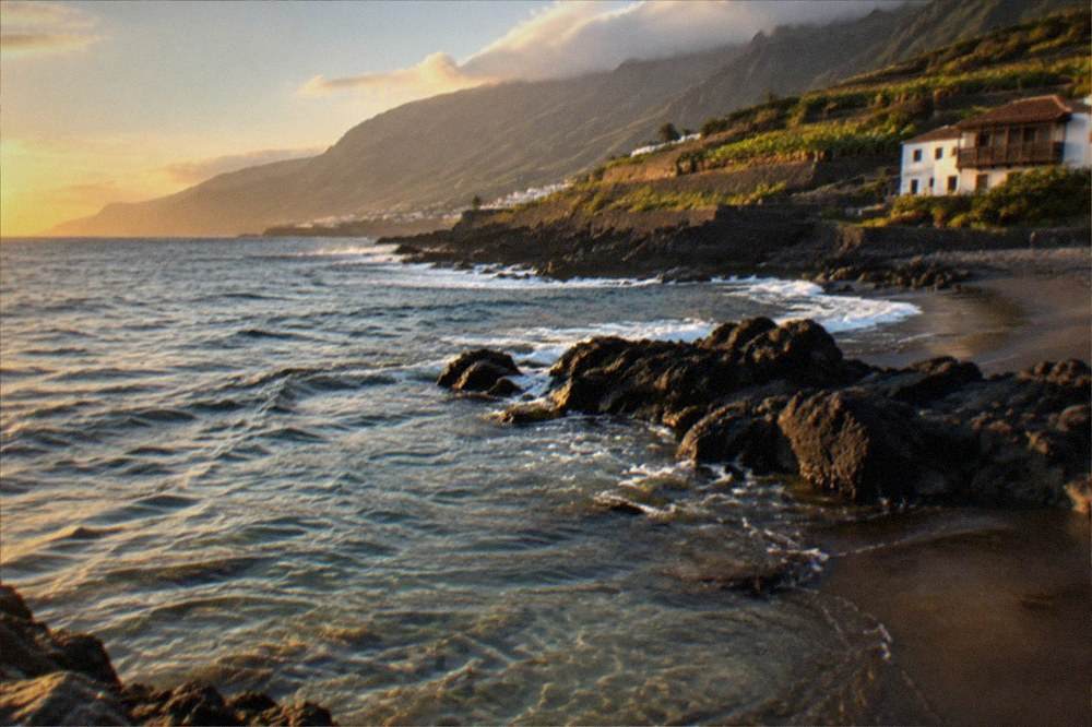 Clear water over dark sand with rocky patches and small fish near the shore