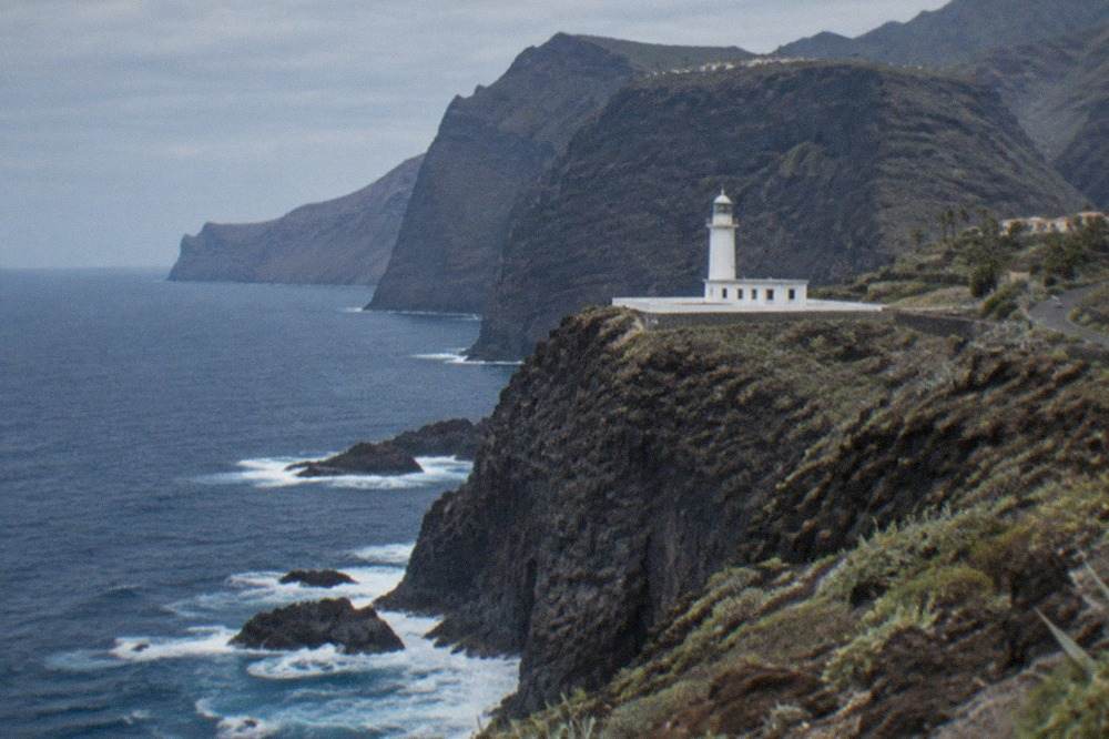A white lighthouse on a rocky headland above dark volcanic cliffs and the open Atlantic