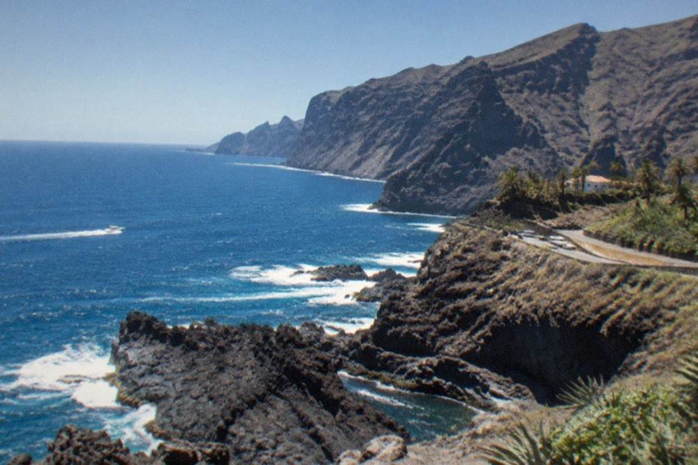 Dark volcanic rocks at the water's edge with waves breaking against the headland