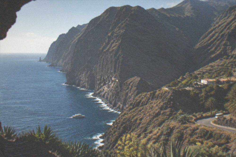 Tall dark sea cliffs rising from blue water with a small boat beside them for scale