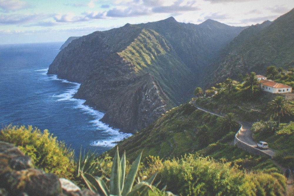 Green hillsides with terraced fields sloping towards the sea under scattered cloud