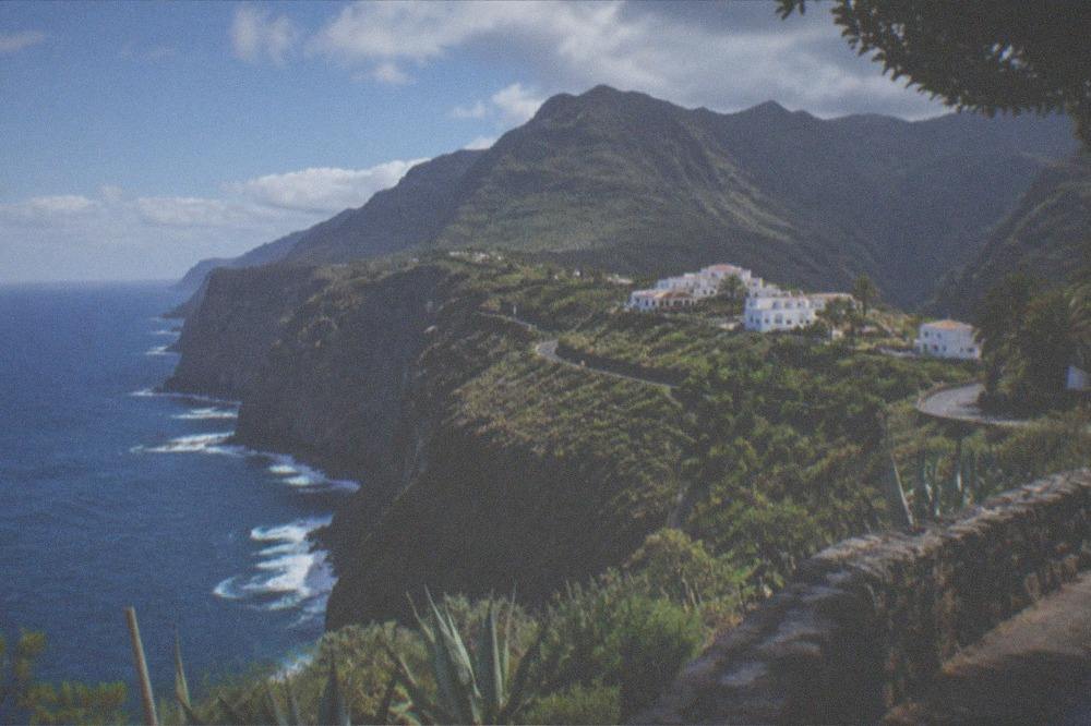A small whitewashed village on a green ridge with mountains rising behind it