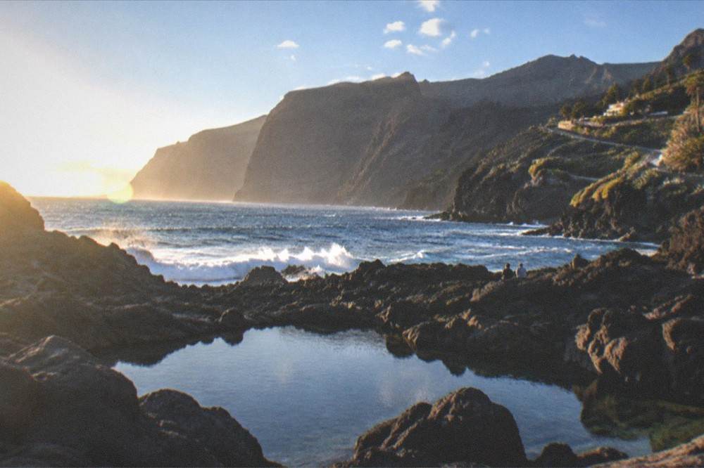 A rocky shoreline with dark stone natural pools and waves breaking beyond them