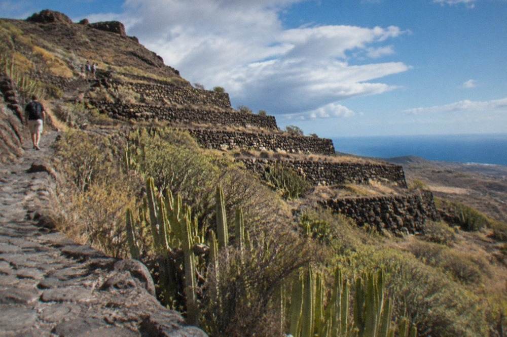 Stepped stone terraces rising from a volcanic slope under a blue sky