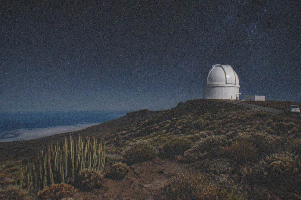 A white telescope dome on a mountain ridge above the clouds