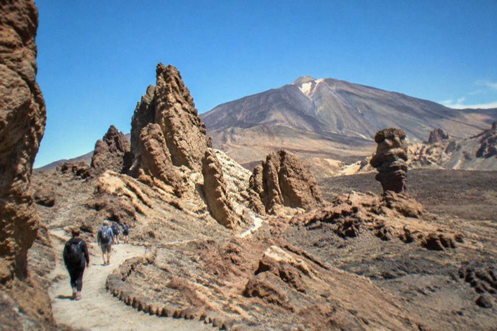 Visitors walking a rocky path among stone towers at the Roques de Garcia under a clear sky