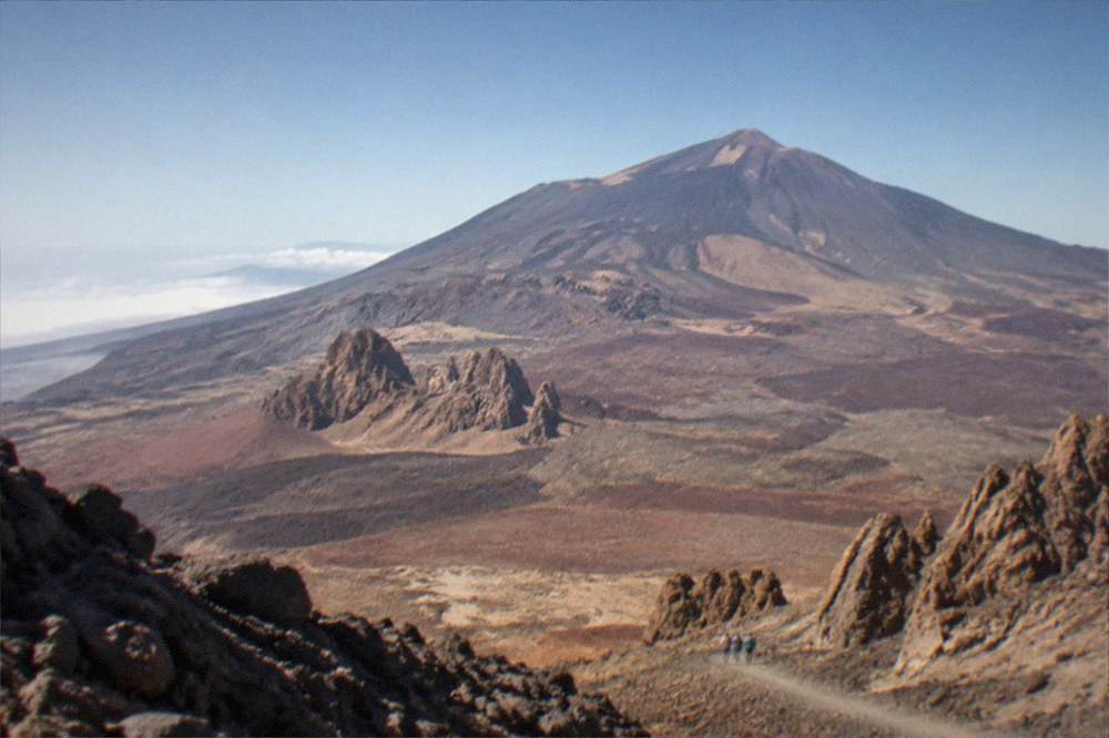 A sign beside a rocky trail in Teide National Park with volcanic terrain stretching behind it