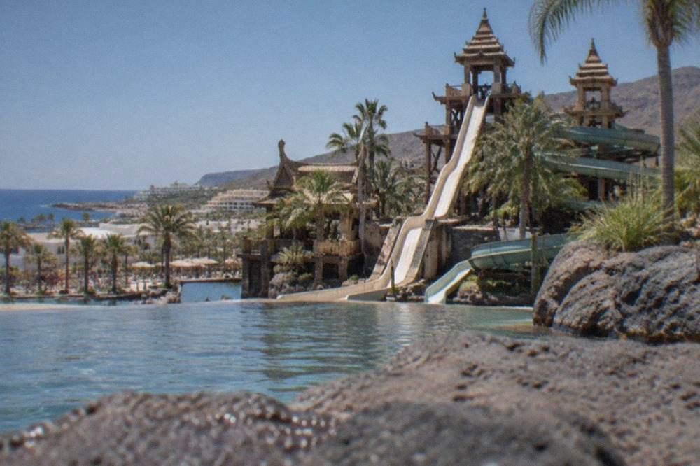 A Thai-themed water park with palm trees, towers and slides under a blue sky in Costa Adeje, Tenerife