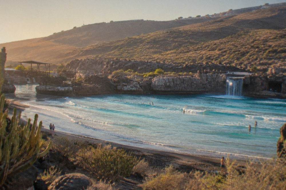A wide view of a water park lagoon with a wave machine beach and rocky landscaping