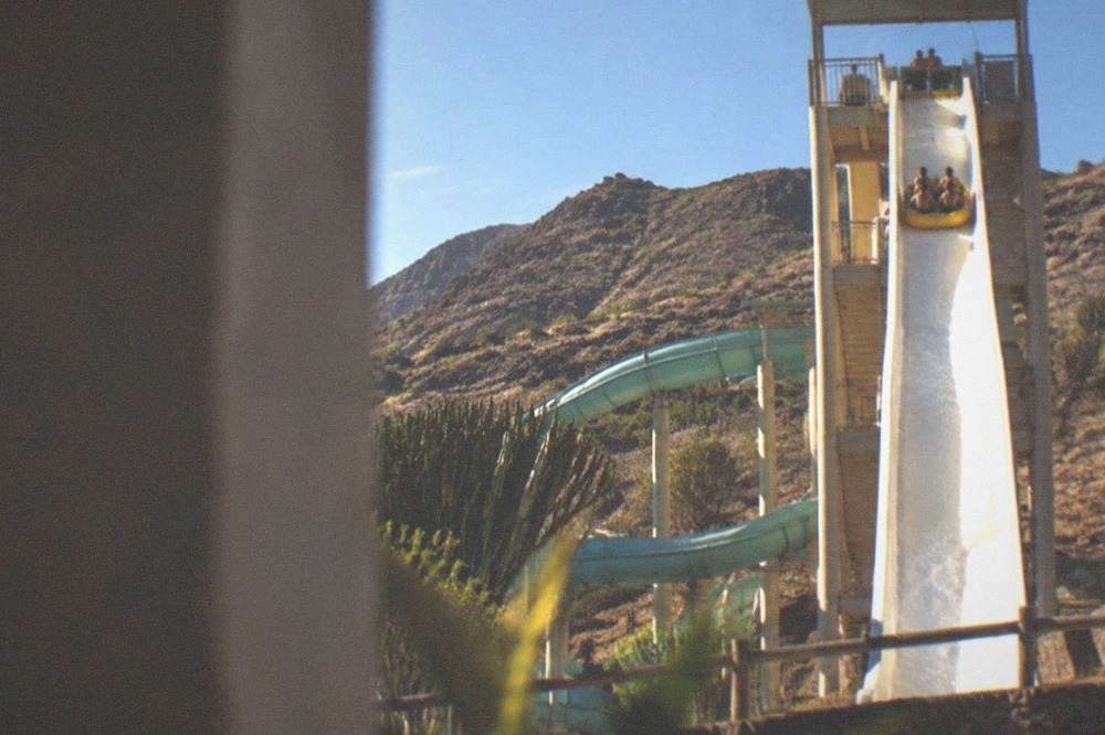 A water slide tower with a steep drop and riders in the foreground of a bright day