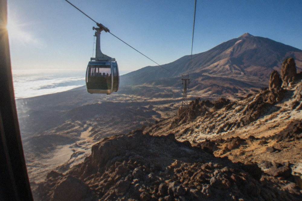 A cable car cabin travelling above a rocky volcanic slope under a clear sky