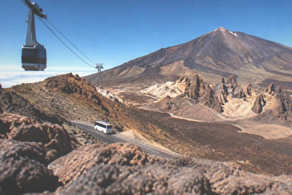 A coach parked on a winding road below a large volcanic cone