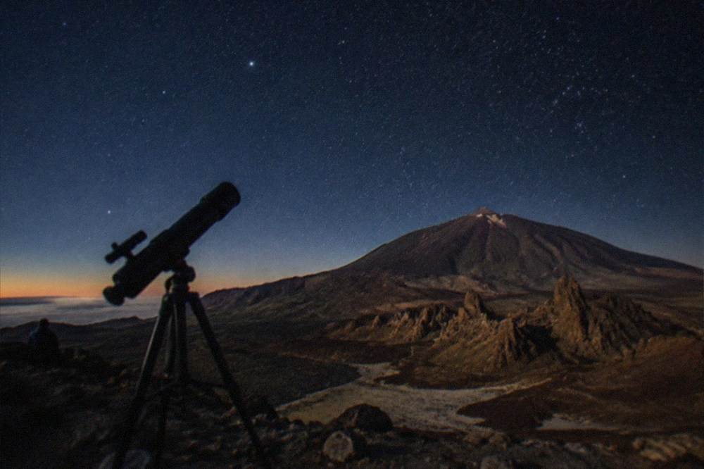 A telescope silhouetted against a star-filled night sky above Teide National Park