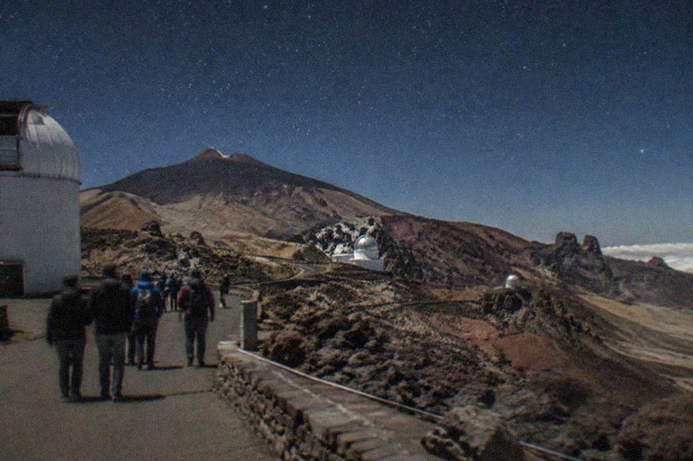 A small group of visitors walking between telescope domes with a guide on a paved observatory path