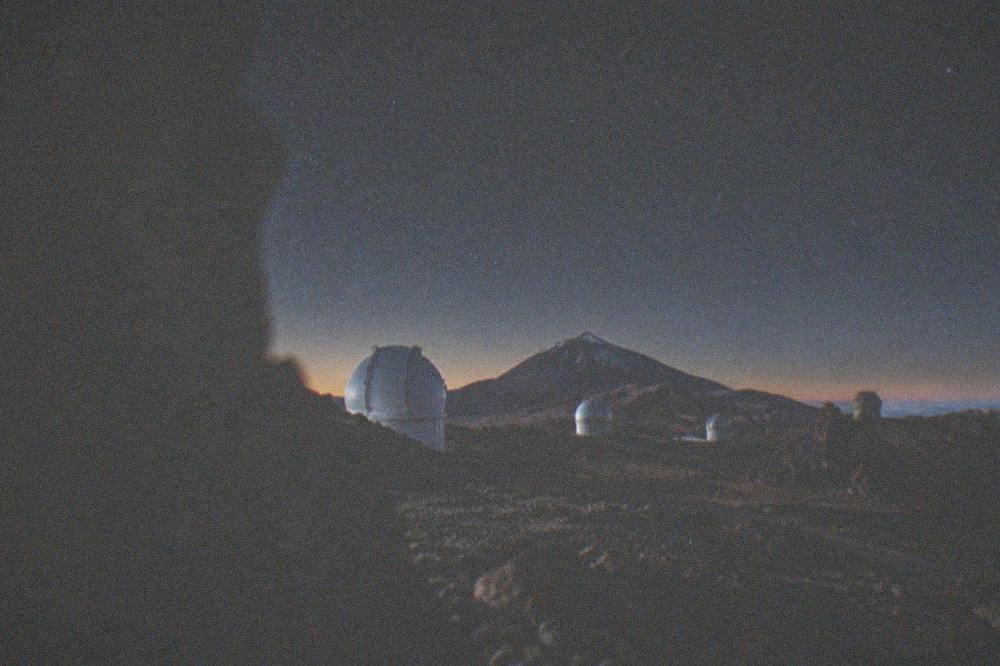 Telescope domes of the observatory seen across volcanic rock with Teide's summit in the distance