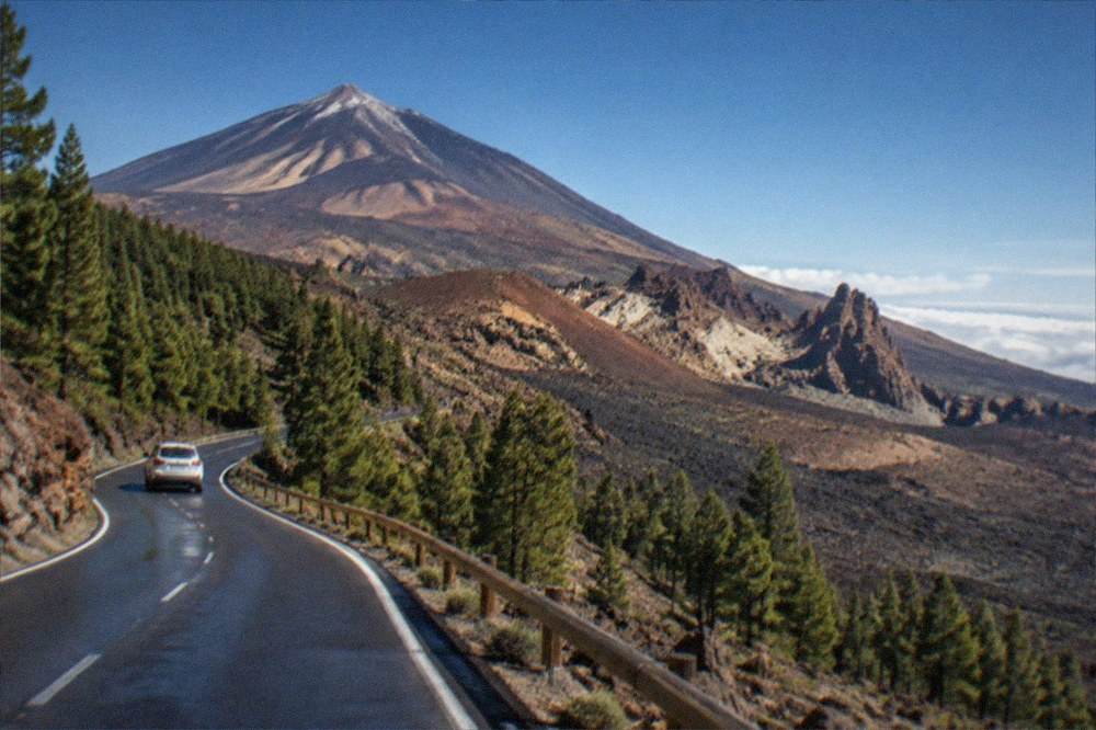 A road winding up through pine forest toward the observatory ridge with Teide in the background