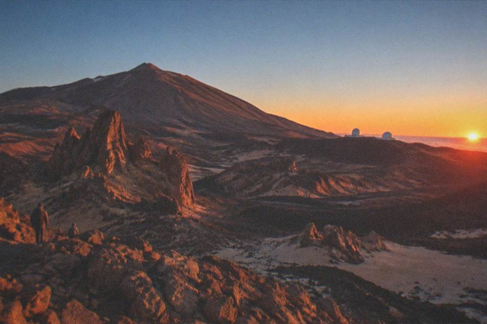 Sunset light over the volcanic landscape of Teide National Park with observatory domes on the horizon
