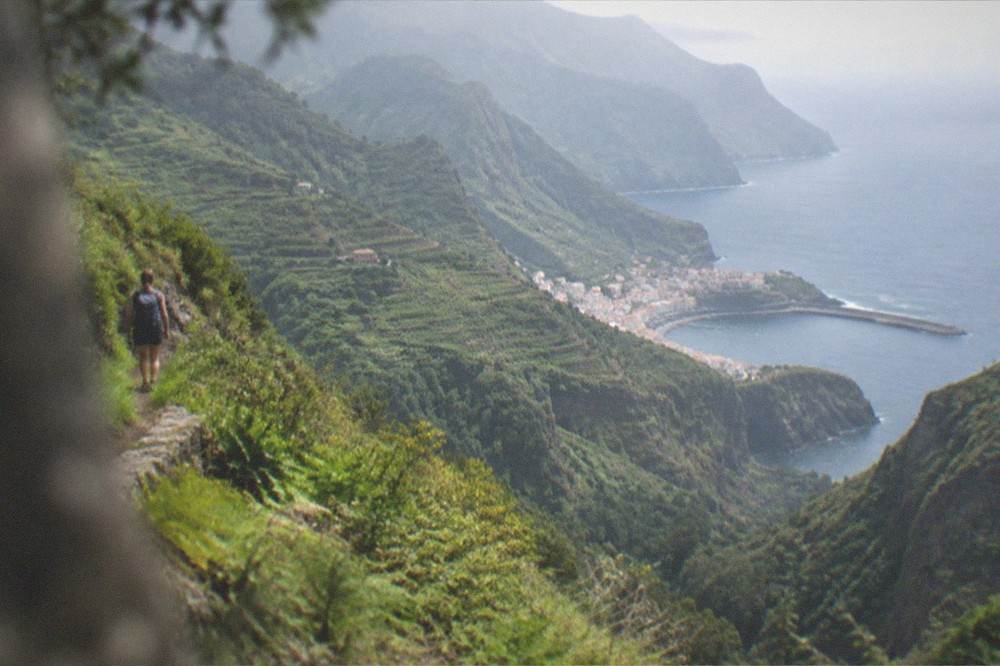 Hiker on a narrow green trail above a deep ravine
