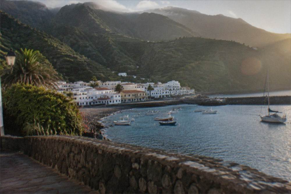 Small white town by a harbour with green mountains behind it