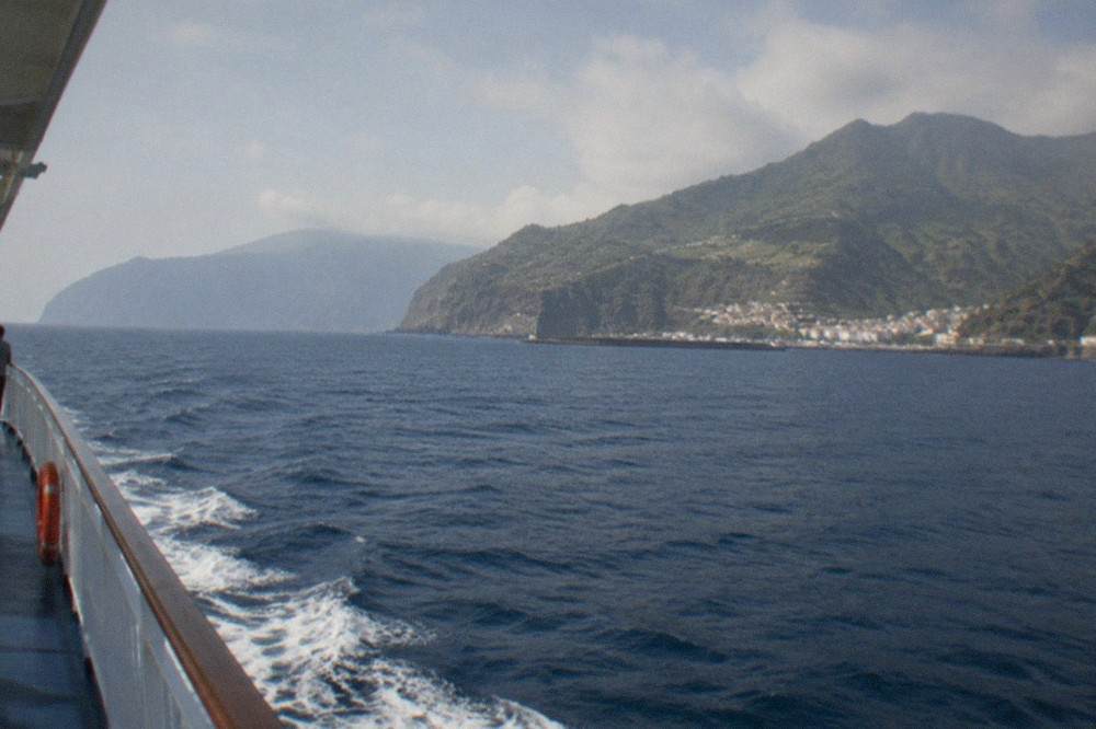 A ferry sailing on open Atlantic water towards a green volcanic island