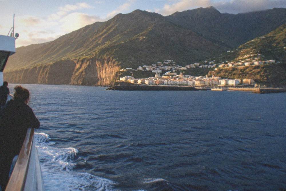 A ferry approaching a volcanic island coastline in late afternoon light