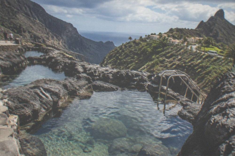 Dark volcanic rock pools filled with clear seawater along a seafront promenade